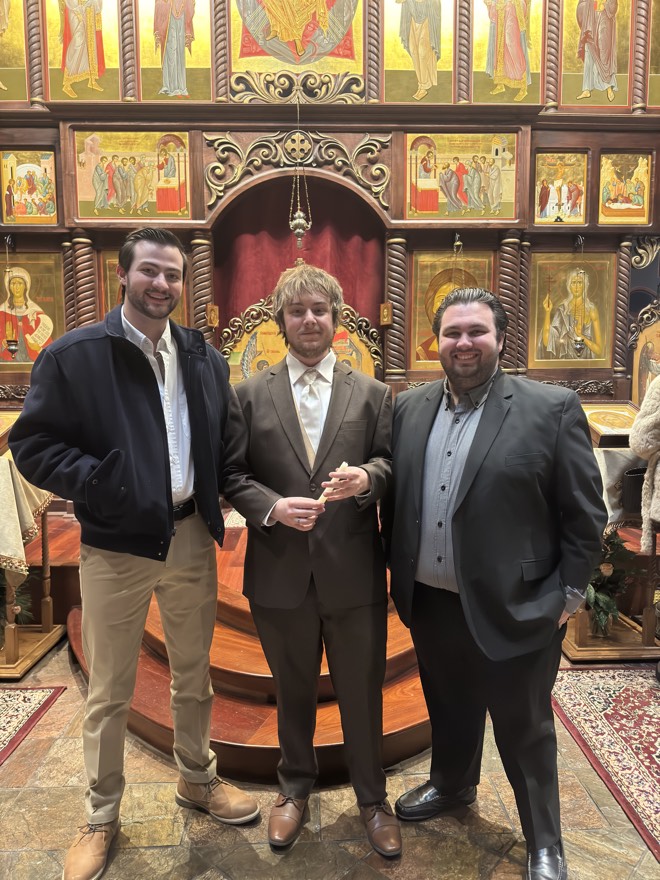 Bibby in a grey suit with two friends in front of a wall of icons in a church