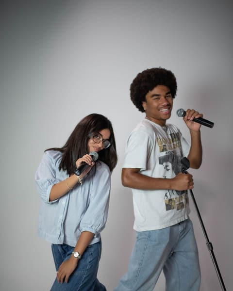 Two friends hamming it up with microphones, one leaning on a mic stand mid-song.