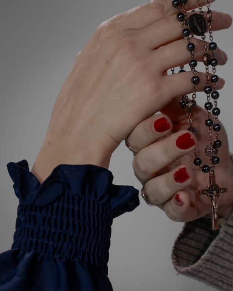 Close-up of two hands holding a dark rosary, one with red nail polish.